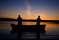 Two people on a boat fishing at sunset